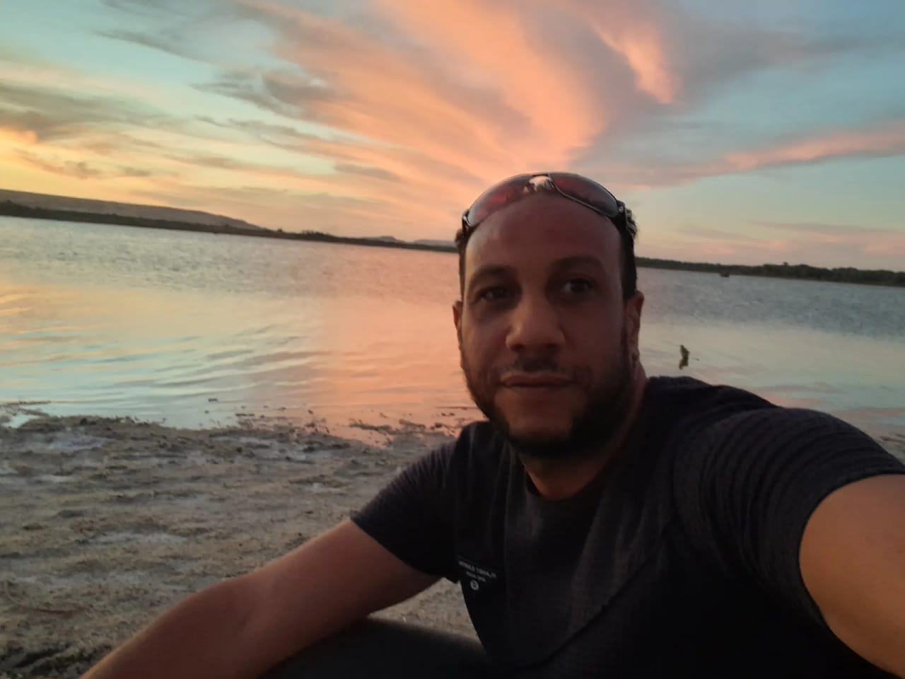 Yasser at a desert salt lake under a pink sunset sky